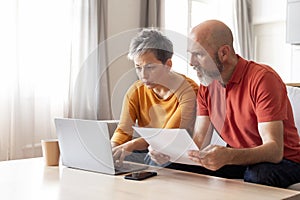 Portrait Of Serious Mature Spouses With Laptop Doing Paperwork Together