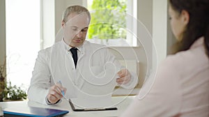 Portrait of serious mid-adult doctor looking through patient`s examination results and shaking head. Caucasian physician
