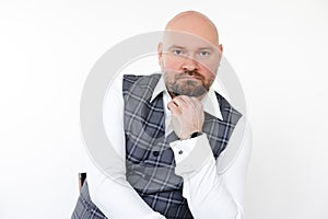 Portrait of serious middle-aged businessman in grey vest, white shirt sitting, putting chin on hand on white background.