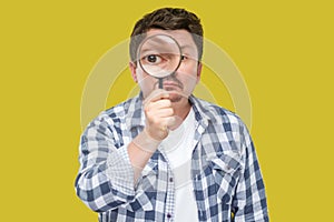 Portrait of serious middle aged man in casual checkered shirt standing, holding magnifying glass and looking at camera with big