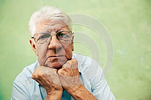 Portrait of serious old man looking at camera with hands on chin