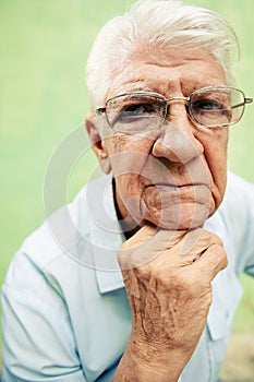 Portrait of serious old man looking at camera with hands on chin