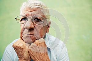 Portrait of serious old man looking at camera with hands on chin