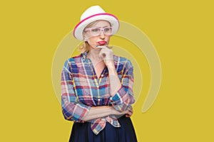 Portrait of serious pensive modern stylish mature woman in casual style with hat and eyeglasses standing, looking away and