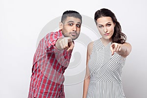 Portrait of serious proud handsome man in red checkered shirt and beautiful woman in white striped dress standing, pointing and