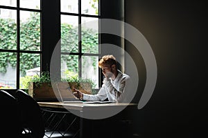 Portrait of serious readhead bearded business man holding smartphone, sitting at workplace