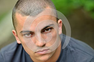 Portrait of serious and sad handsome young man outdoors in nature, looking to camera. Expressive face