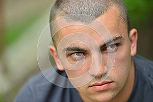 Portrait of serious and sad handsome young man outdoors in nature, looking to a side