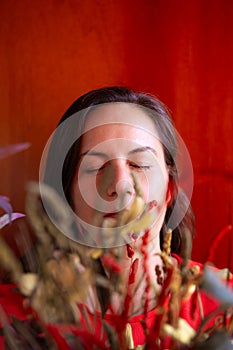 Portrait of serious, sad and pensive 50-year-old woman with closed eyes on red background and dried flowers