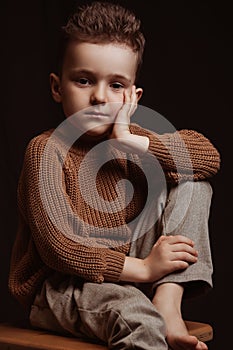 Portrait of serious sad stylish white caucasian child boy kid preschooler a chair