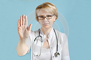 Portrait of serious senior female doctor, beautiful adult woman in medical uniform with stethoscope,  showing stop gesture with he