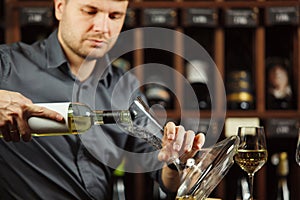 Portrait of serious sommelier pouring white wine in decanter