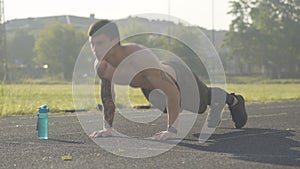 Portrait of serious sportsman training at sunrise on stadium. Side angle view of concentrated Caucasian man pushing up