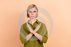 Portrait of serious strick dissatisfied girl with short hair dressed green shirt holding arms crossed  on pastel