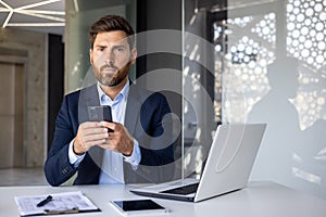 Portrait of a serious and successful young businessman, boss and director sitting in the office at the desk, holding the