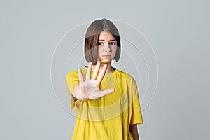 Portrait of a serious teen girl showing stop, ban, block gesture, standing over light grey background. No, Stopping