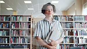 Portrait of serious teenage boy walking in school library with books alone