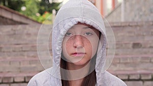 Portrait of serious teenage girl with freckles, wearing grey hoodie, in suburban setting.