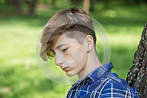 Portrait of serious teenager sitting on grass in park. Gen Z. Unhappy and stress