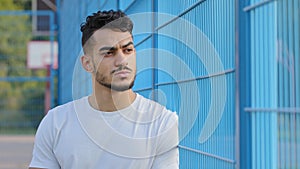 Portrait of serious tense focused Middle eastern indian football fan watching soccer match through netting, fence. Young