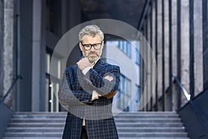 Portrait of serious thinking mature businessman, senior gray haired man in business suit outside office building