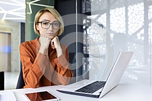 Portrait of a serious thinking woman inside the office at the workplace, business woman looking focused at the camera