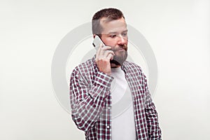 Portrait of serious upset bearded man talking on cell phone, looking aside with gloomy dismal face. white background