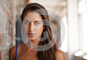 Portrait, serious and woman by brick wall for confidence or casual fashion in corridor alone. Face, skin or young