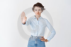 Portrait of serious woman looking angry, frowning and stretch out hand in stop gesture, say no, forbid action, standing