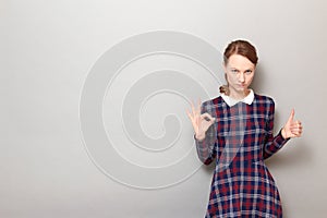 Portrait of serious woman showing okay gesture, giving thumb up sign