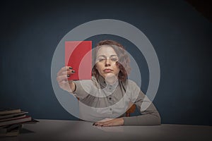 Portrait of serious woman teacher with books pointing red card as symbol of failed exam by a student