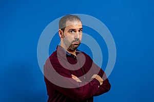 Portrait of serious and worried spanish bearded man with crossed arms, isolated on blue studio background