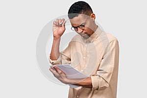 Portrait of serious young African student man in beige shirt analyzing reports posing on white studio background. Pensive male