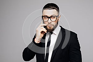 Portrait of serious young attractive man in black suit talking on mobile phone on gray background