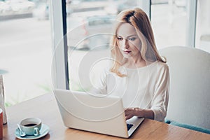 Portrait of serious young blond lady entrepreneur lawyer, in white formal wear, sitting at her work place in a coworking and