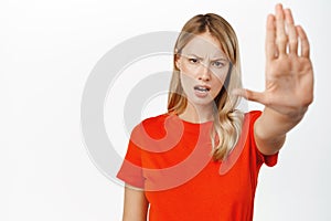 Portrait of serious young blond woman say stop, showing taboo, block refusal gesture, extending one arm forward