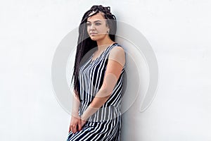 Portrait of serious young brunette woman with black afro american dreadlocks hairstyle in striped dress, standing and looking away