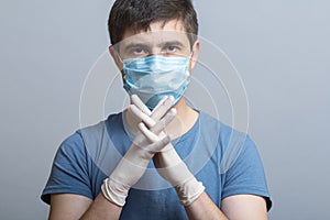 Portrait of a serious young doctor in protective medical mask in surgical gloves ready to operate on gray studio background,