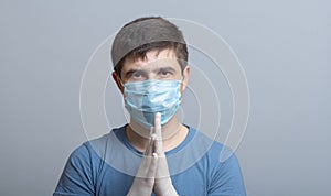 Portrait of a serious young doctor in protective medical mask in surgical gloves ready to operate on gray studio background,