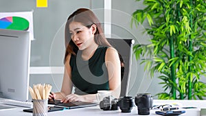 Portrait of serious young female photographer sitting in her studio, looking at the monitor and focusing on retouching and editing