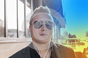 Portrait of a serious young guy of European appearance, an attractive businessman in sunglasses, listening to music in headphones