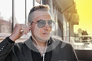 Portrait of a serious young guy of European appearance, an attractive businessman in sunglasses, listening to music in headphones