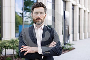 Portrait of a serious young man, a businessman, a lawyer standing in a business suit outside an office center, looking