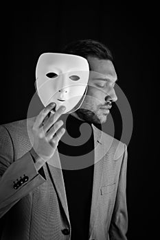 Portrait of a serious young man holding a white mask in his hand, concept for being authentic