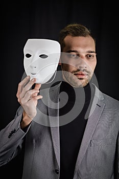 Portrait of a serious young man holding a white mask in his hand, concept for being authentic