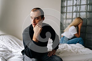 Portrait of serious young man pensive looking away not talking after dispute with sad wife sitting apart on bed