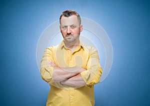 Portrait of serious young man, strict guy with hands on waist looking to camera over blue background, dresses in yellow shirt
