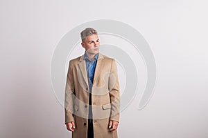 Portrait of serious young man in a studio, wearing brown coat. Copy space.