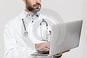 Portrait of serious young medical doctor with stethoscope working in clinic and holding laptop