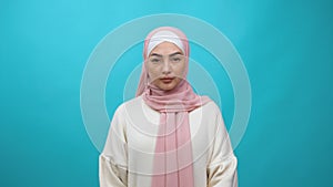 Portrait of serious Young Muslim woman in hijab standing calm emotionless, looking at camera with attentive unsmiling